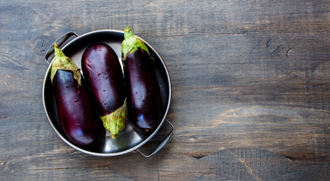 Flat metal pot with 3 eggplant on wood background